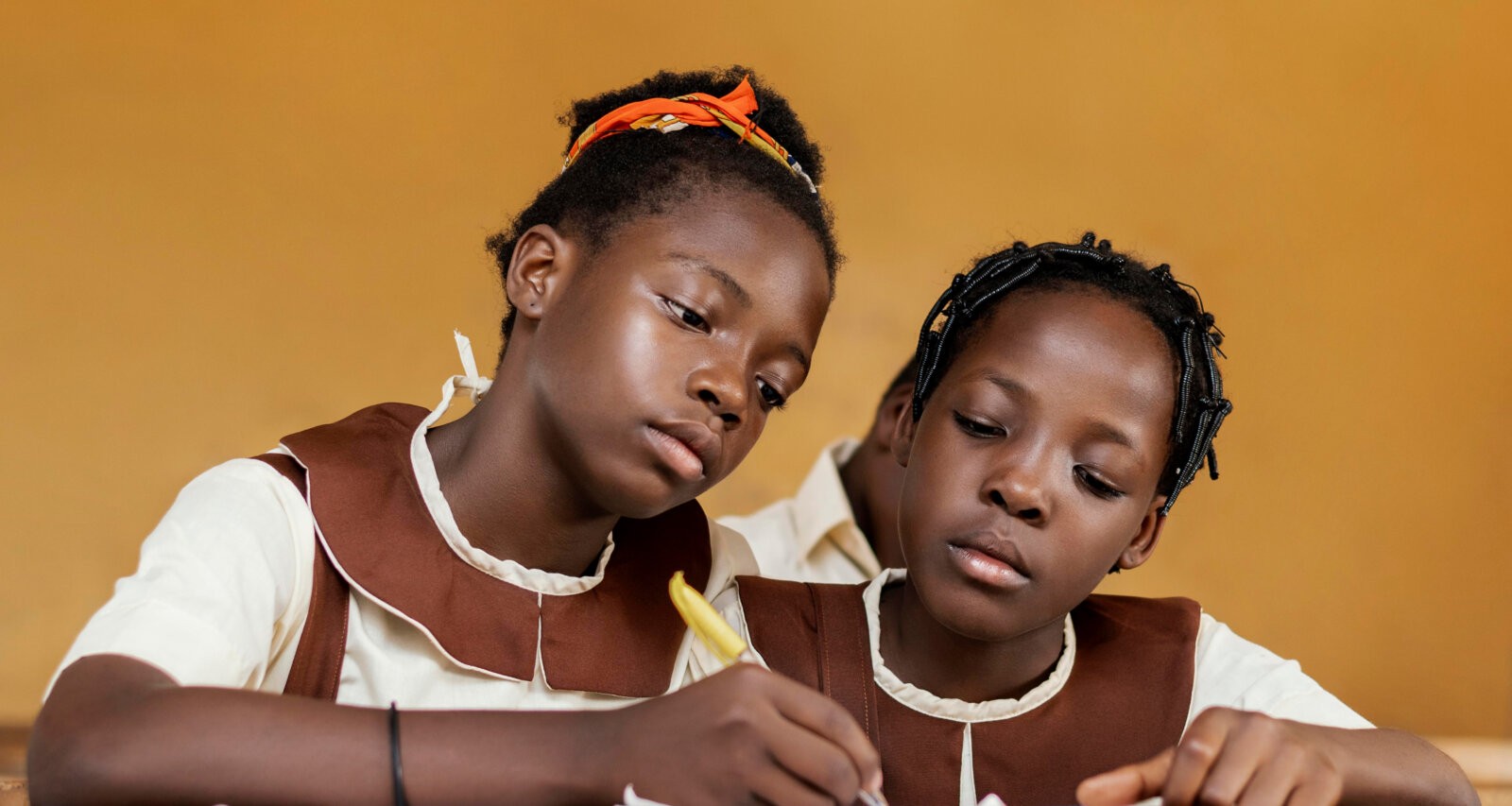 Two girls in uniform writing in a book via Freepik