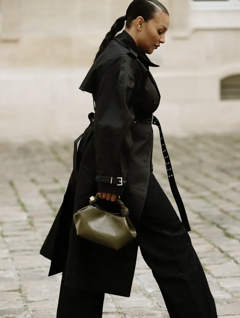 A PFW guest wearing a sleek ponytail with braided ends, and it looks even better with her classic trench coat via Launchmetrics.com