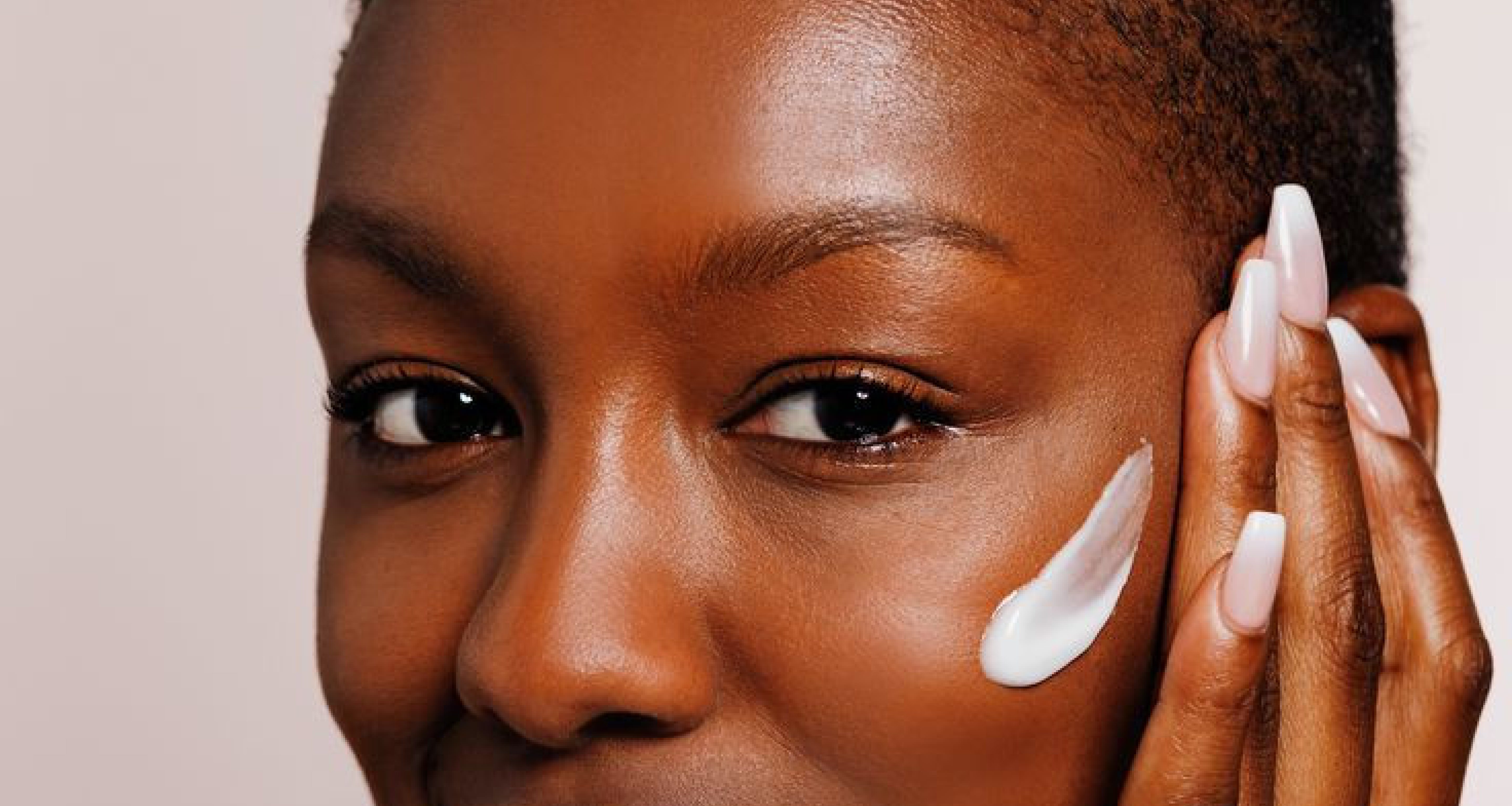 A dark skinned woman with a moisturiser swatch on her right cheek