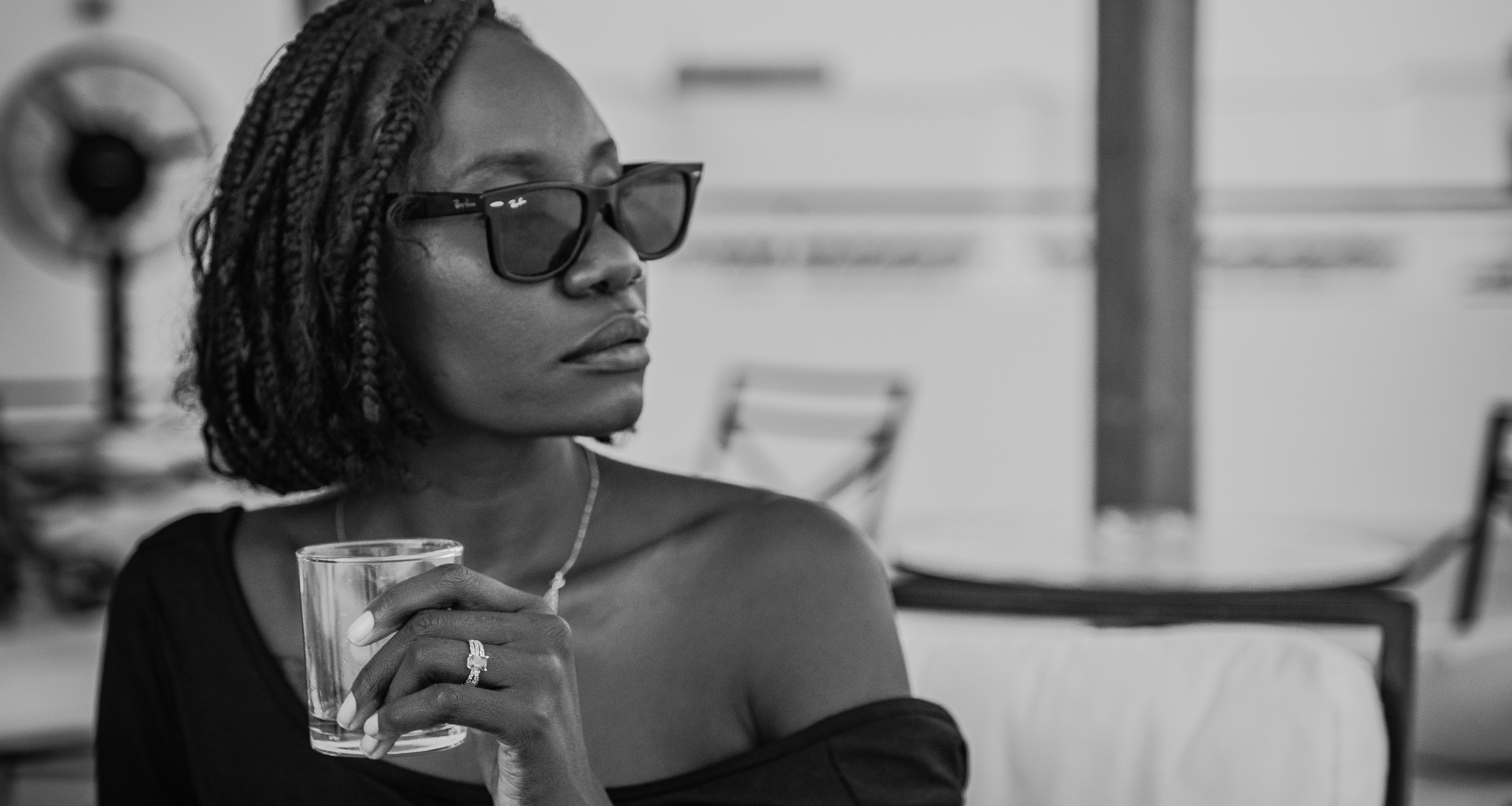 Black and white image of a Black woman wearing dark sunglasses and holding a glass by Lisa Marie-Theck via Unsplash