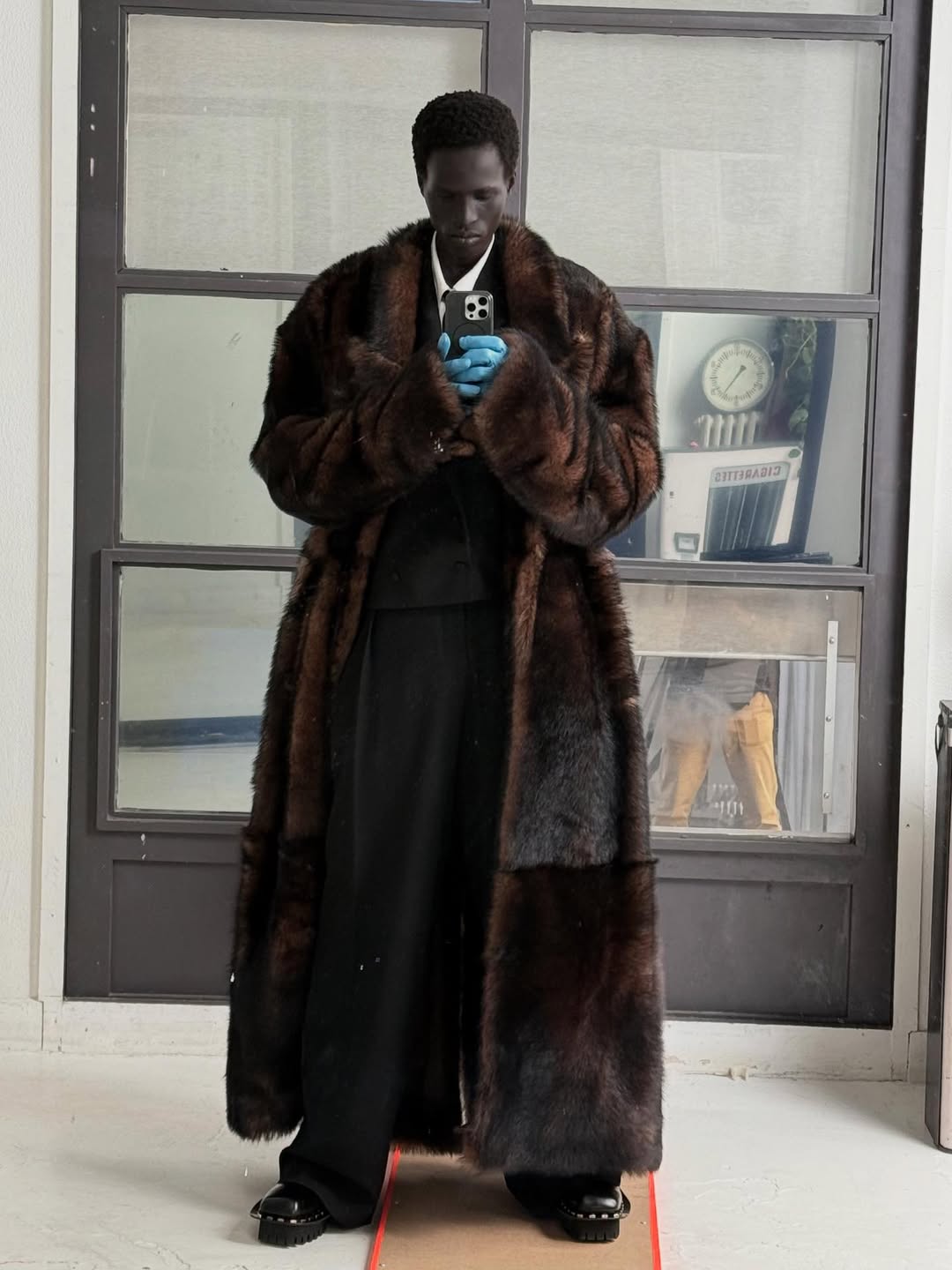 BoF class of 2025; Mamuor Majeng in a black suit and long brown coat standing in front of a mirror